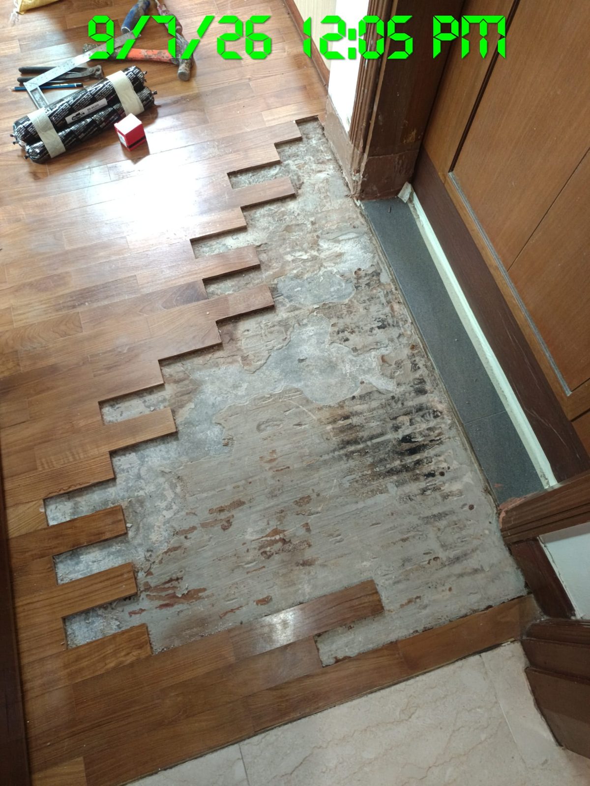 Severely damaged, staggered parquet blocks at a doorway before repair
